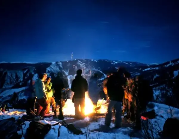 Kashmir winter camping in snow covered valley with bonfire under starry night sky and Himalayan mountain backdrop